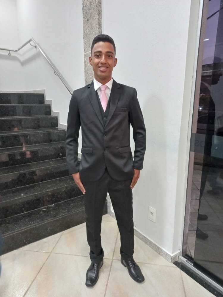 homem sorrindo de terno preto e gravata rosa em um interior com escada de pedra